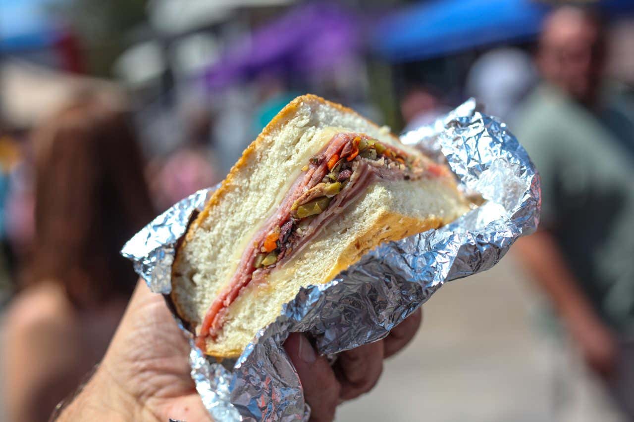 Someone holding a po'boy sandwich in New Orleans, Louisiana, an unexpected culinary destination, the sandwich wrapped in foil