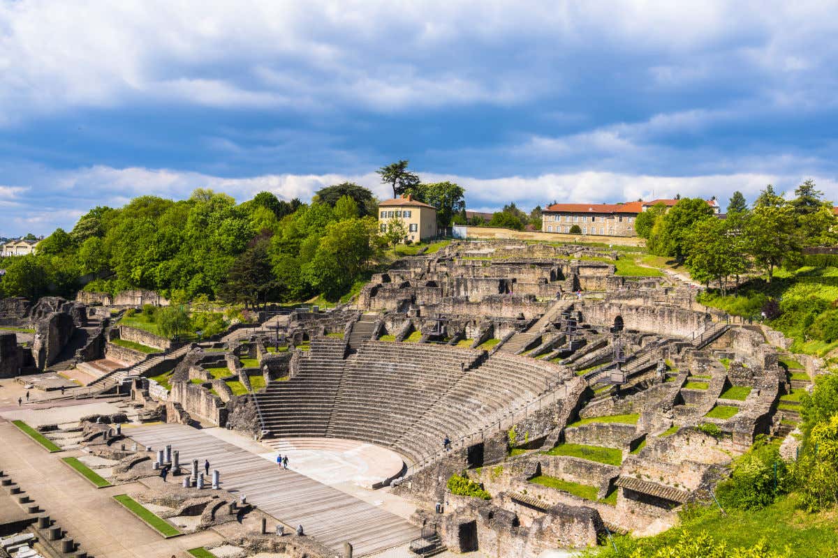 Graderío y escenario de un antiguo teatro romano con varias personas visitando sus ruinas al aire libre