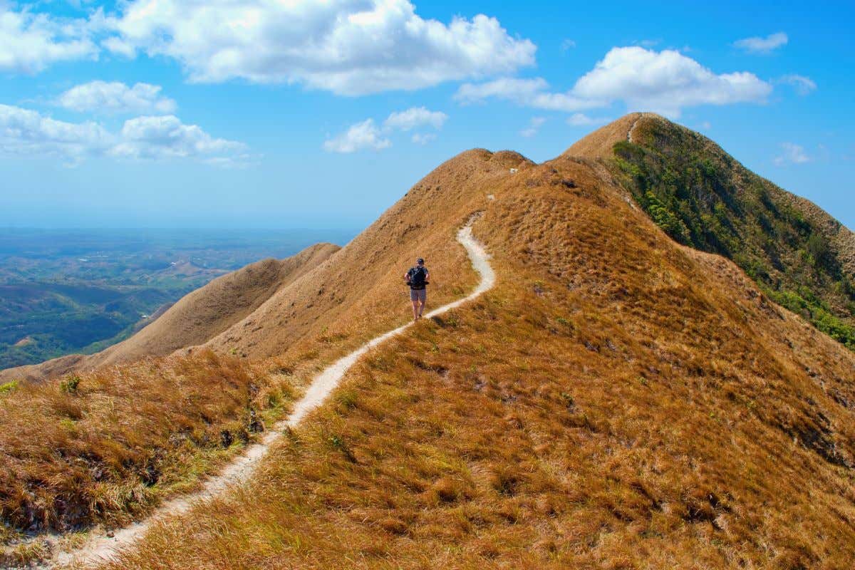 Un hombre caminando por un sendero en lo alto de un cerro árido