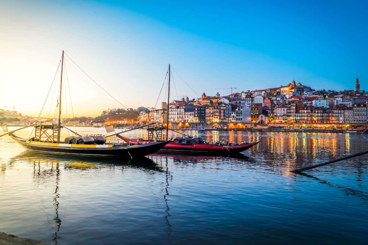 Varios barcos tradicionales navegando al atardecer frente a las coloridas fachadas de las casas de Oporto