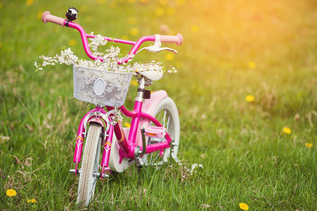Una bicicleta pequeña de color rosa y decorada con unas flores en su cesta