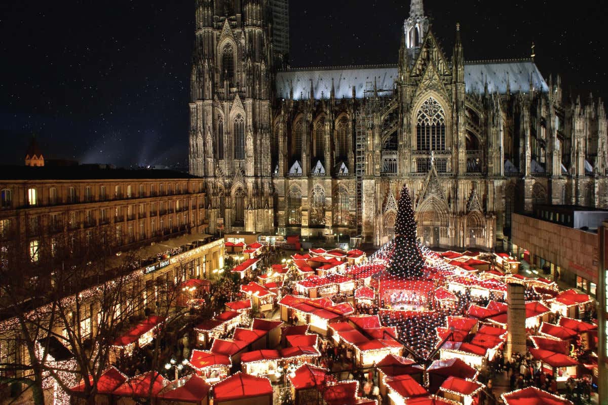 Vista aérea de un mercadillo de Navidad con numerosas casetas de tejados rojizos juntos a la catedral de Colonia