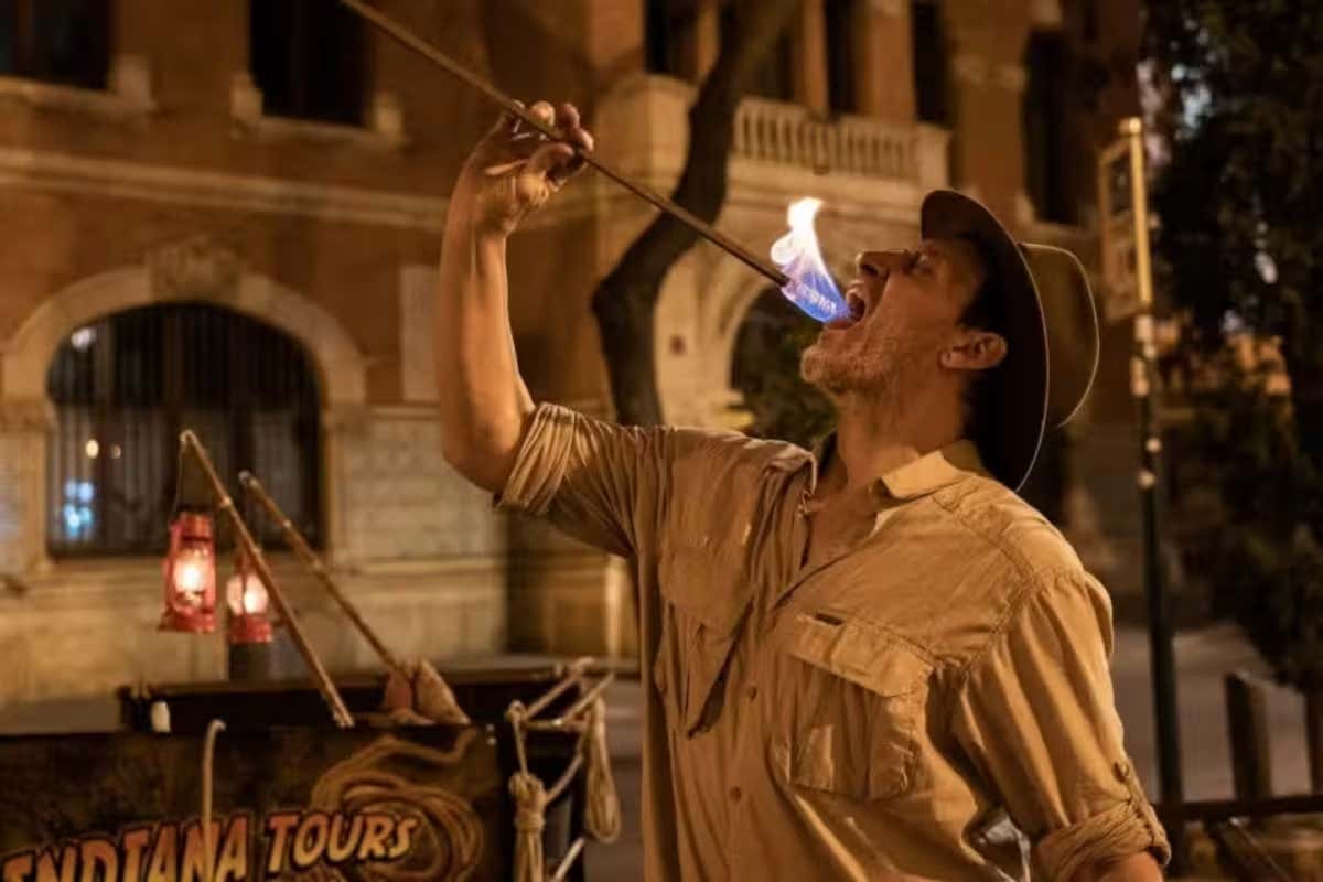 Un hombre disfrazado de Indiana Jones por la noche y tragando una antorcha encendida