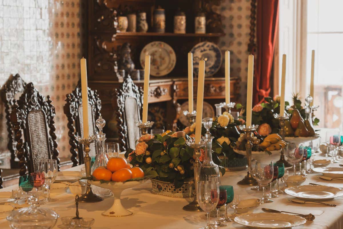 Una mesa elegante decorada con vajilla de lujo y candelabros y rodeada de mesas de madera en el interior de un palacio