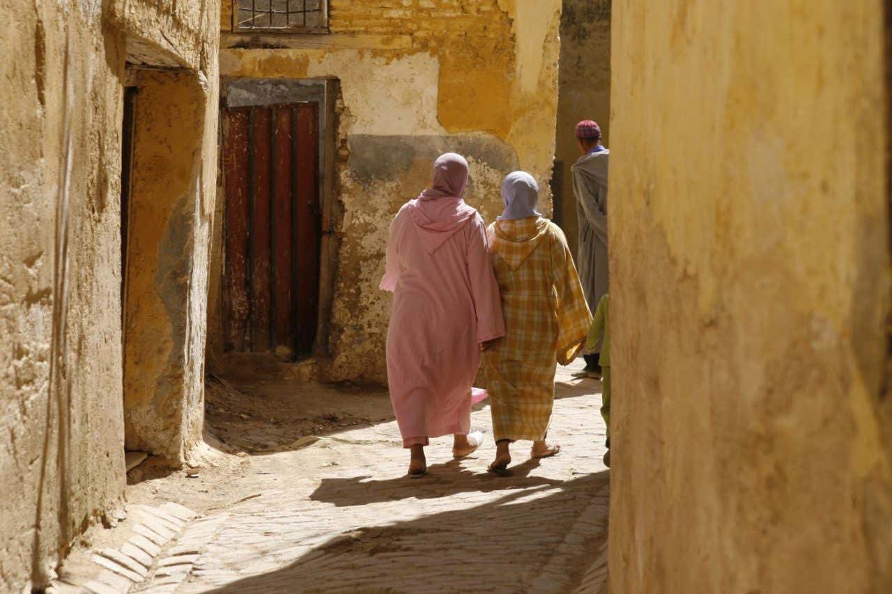 Dos personas con largas ropas caminan en un callejón en una ciudad histórica