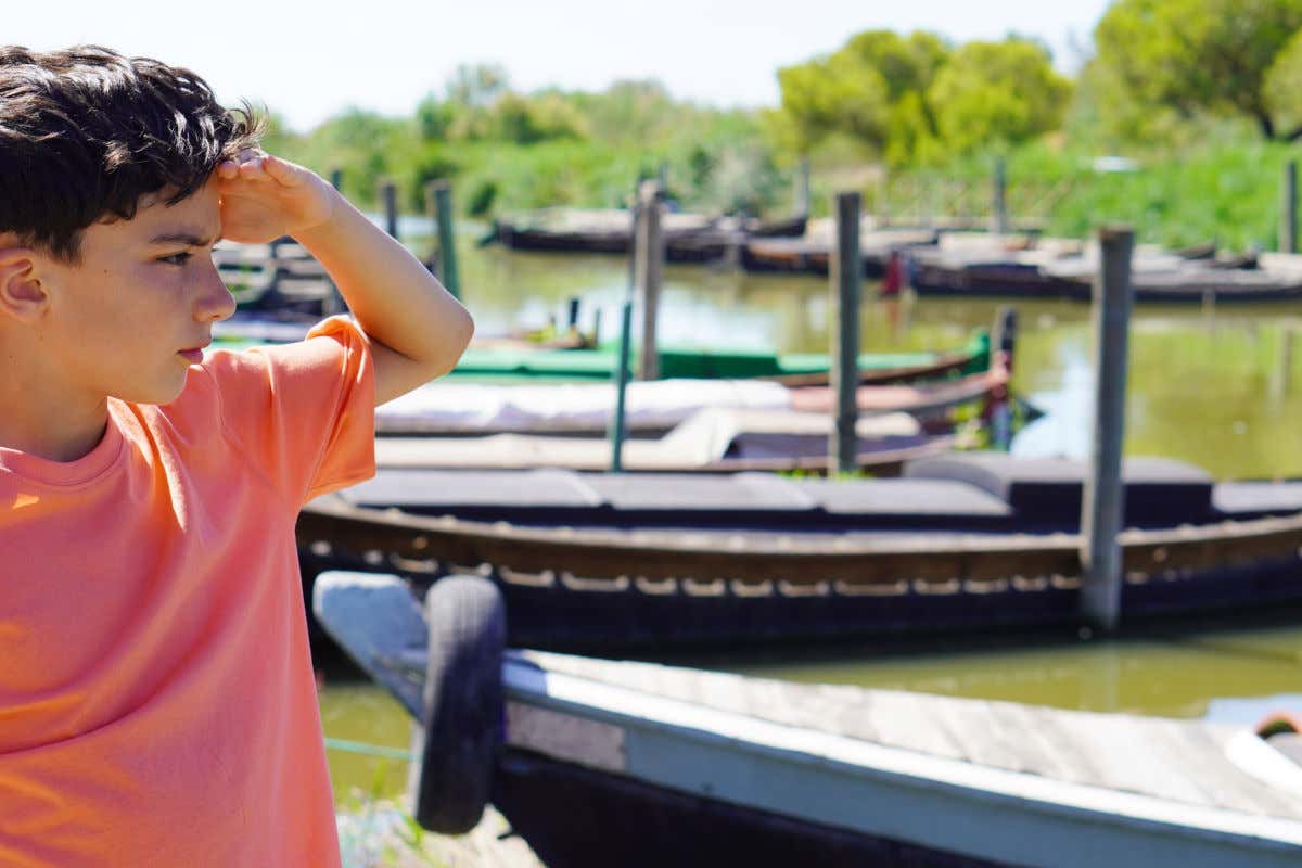 Un niño contemplando varios barcos tradicionales de madera en la Albufera de Valencia