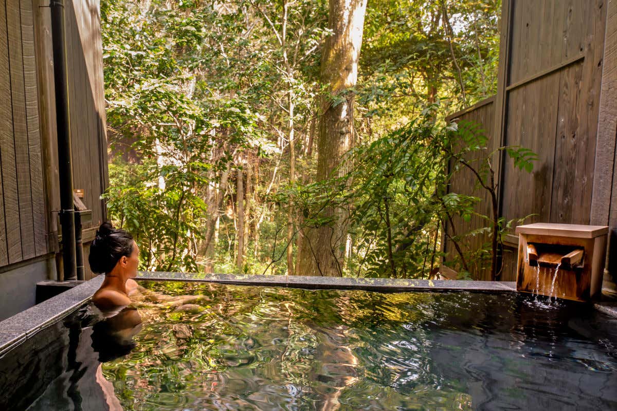 Una mujer tomando un baño en un jacuzzi al aire libre en mitad de un bosque