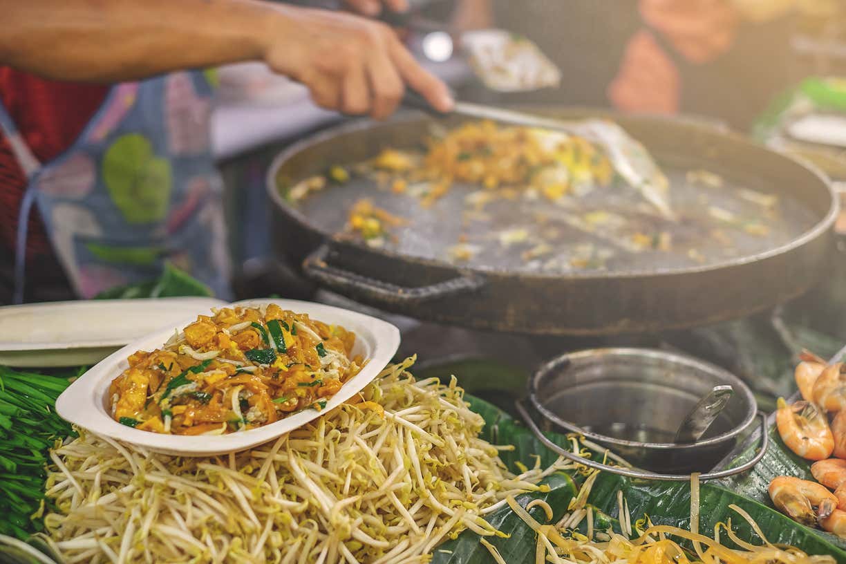 Detalle de unas manos  junto a una sartén preparando un pad thai en un mercado de Bangkok
