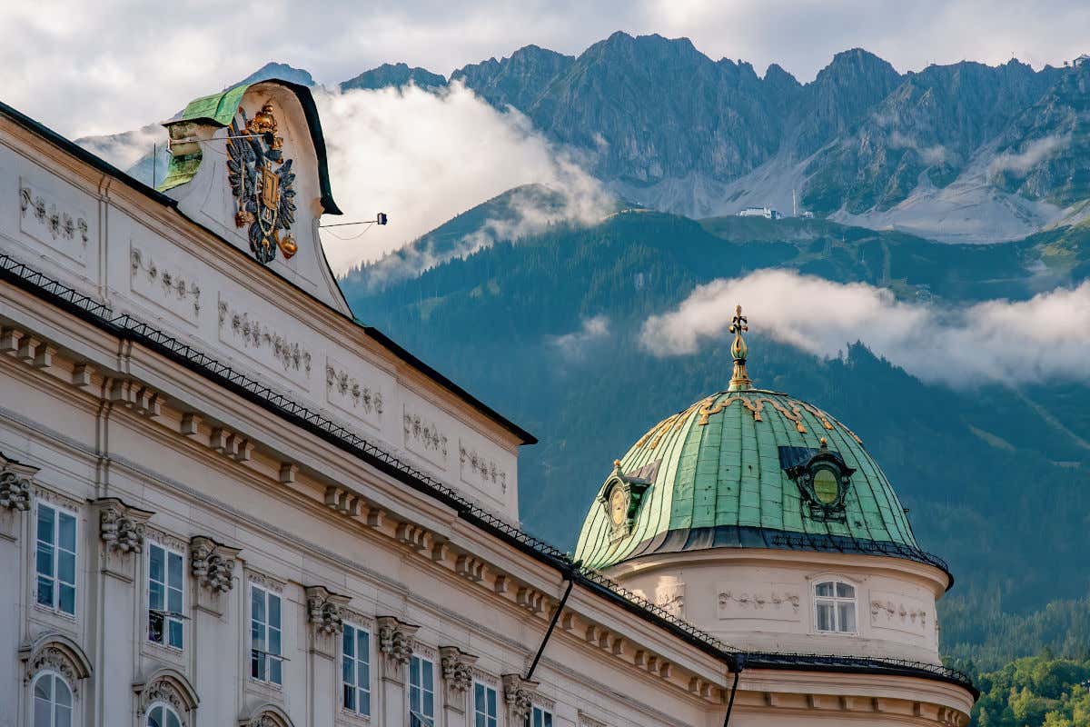 Un palacio decorado con un escudo de armas y una cúpula con vistas a las montañas verdes y nevadas de los alrededores
