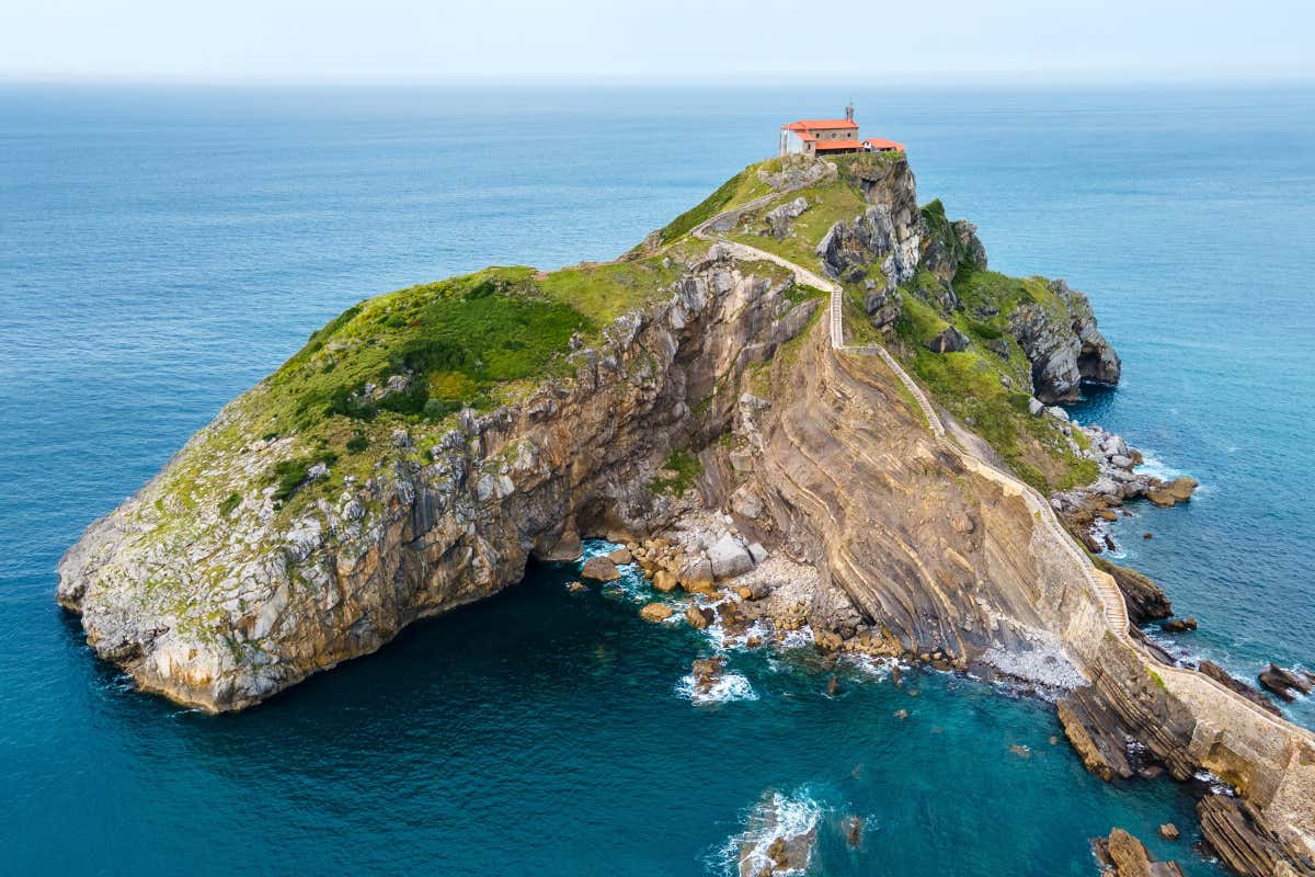 Vista aérea de una isla, con una escalera de piedra ascendiendo hasta una ermita situada en su parte superior