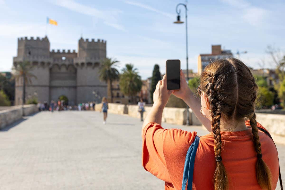 Una joven con coletas de espaldas a la cámara fotografiando con su móvil las Torres Serranas, uno de los monumentos más famosos que ver en Valencia