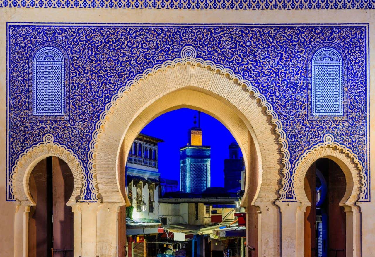 Un arco ornamentado con azulejos azules donde se ve una ciudad al atardecer