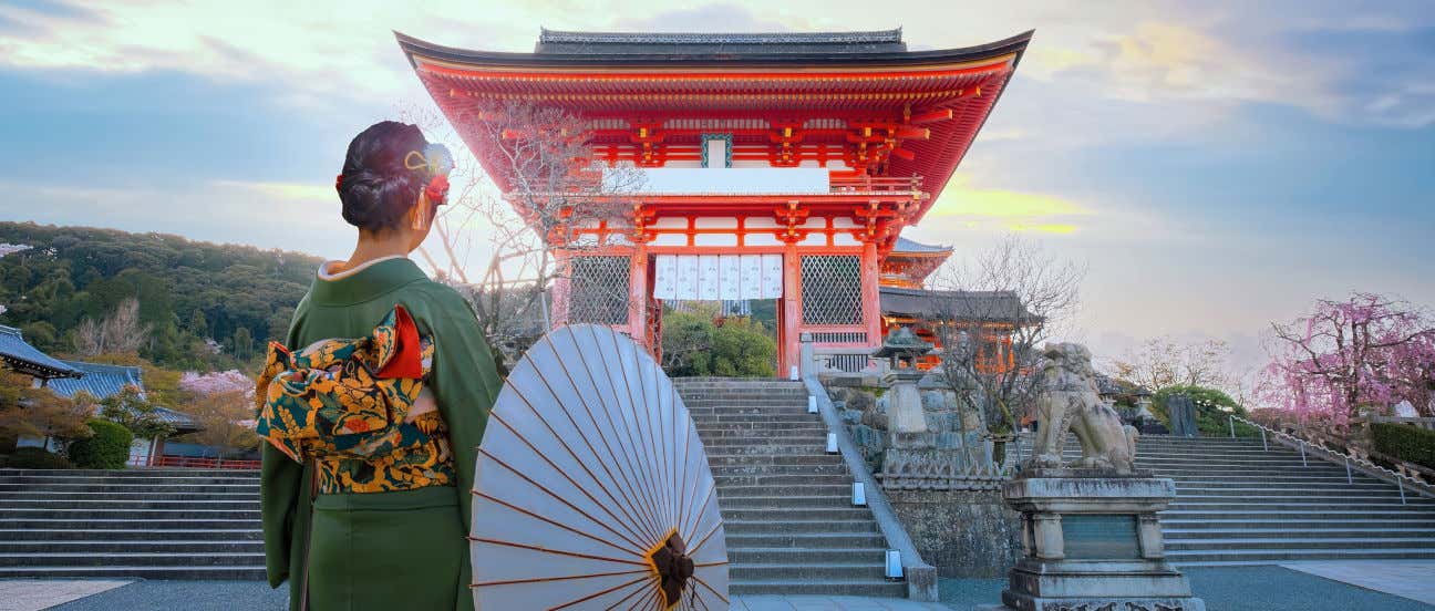 Una mujer con kimono de espaldas a la cámara contemplando un templo de Japón al atardecer
