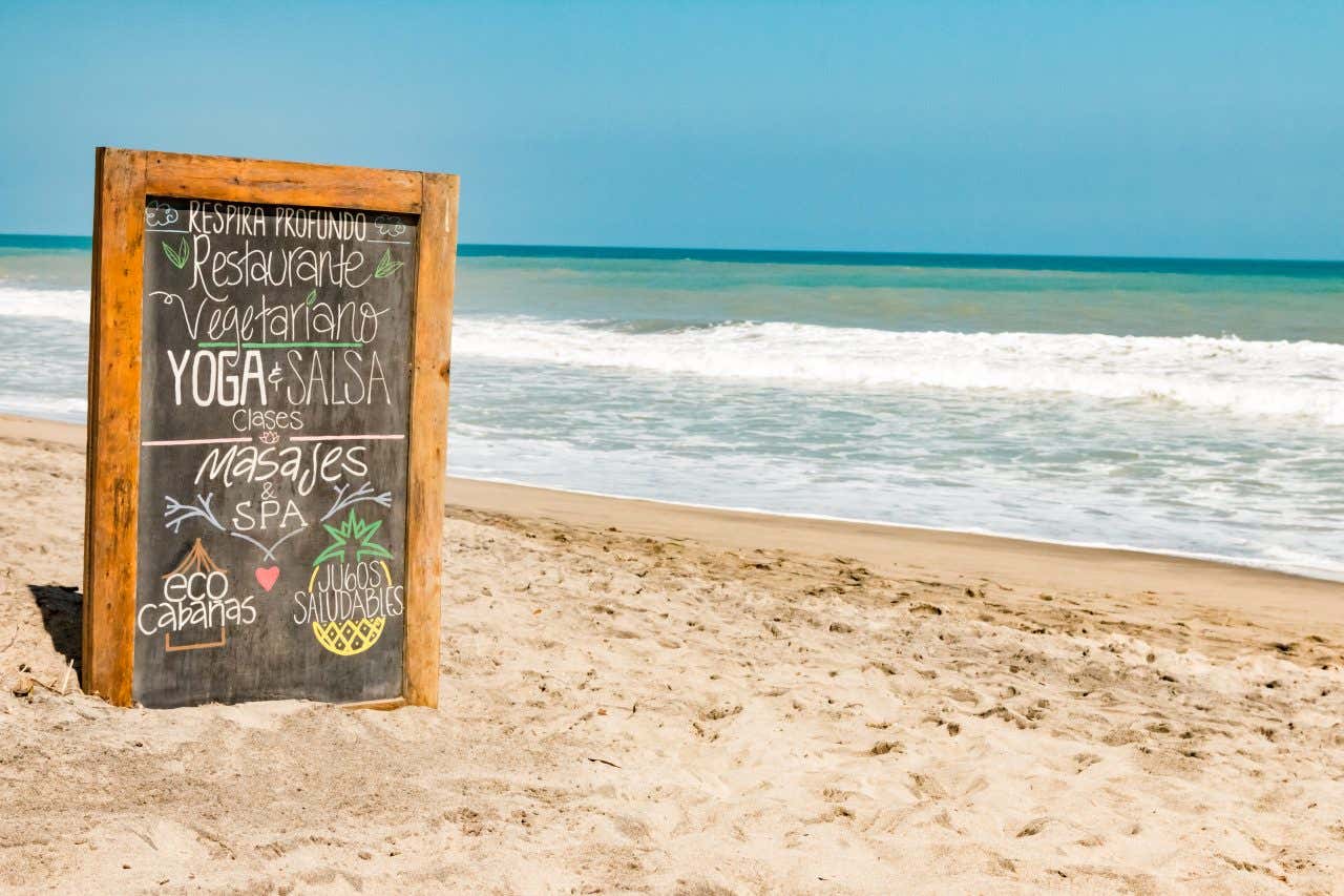 Una lavagna decorata con scritte e disegni sulla spiaggia di Cartagena de Indias, in Colombia. Con questa lavagna i proprietari di un resort invitano i turisti a unirsi ai loro ritiri di yoga e a usufruire dei loro servizi ristorazione
