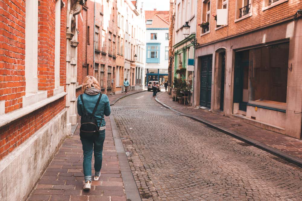 Una donna di spalle cammina su un marciapiede in una stretta via acciottolata del centro storico di Bruges
