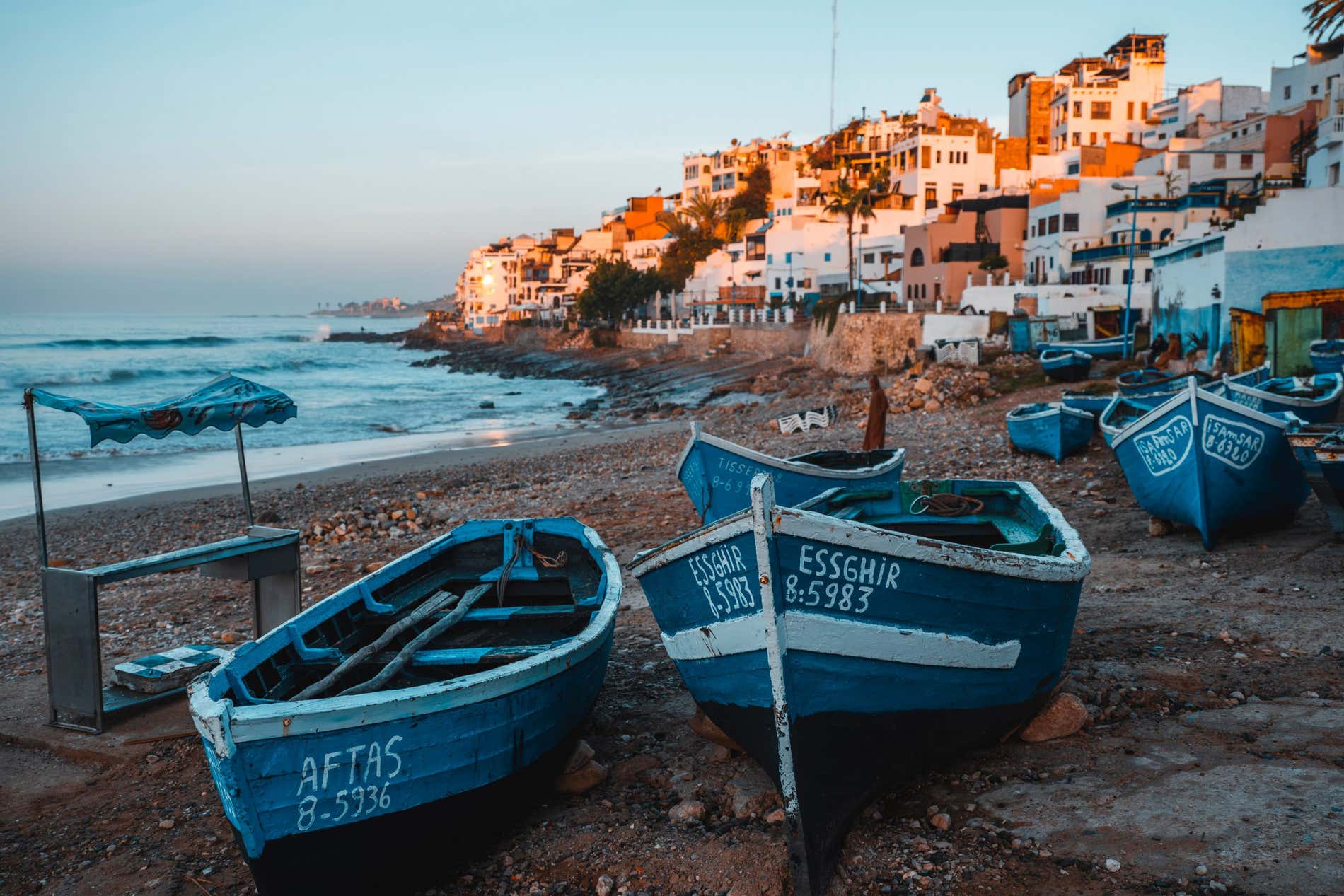 Amanecer en la playa de Taghazout con las casitas de fondo y embarcaciones de pesca en primer plano