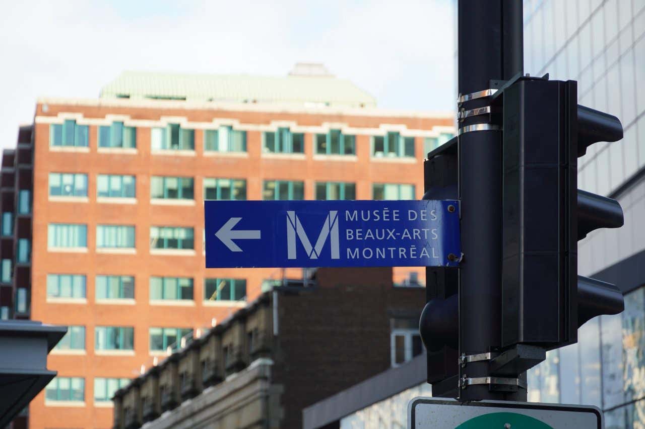 Panneau de signalisation bleu sur des feux tricolores indiquant le Musée des beaux-arts de Montréal, une visite incontournable