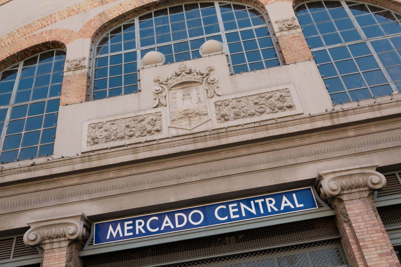 Facciata del Mercado Central di Alicante in stile modernista, con grandi finestre ad arco, dettagli ornamentali in pietra e insegna blu con la scritta 'Mercado Central'