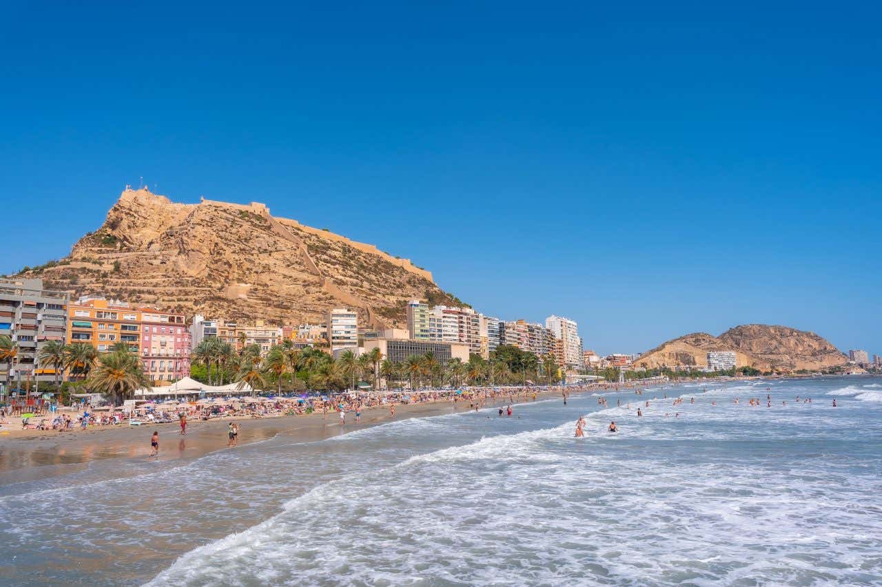 Una spiaggia con diversi bagnanti in una giornata di sole e un monte brullo sullo sfondo