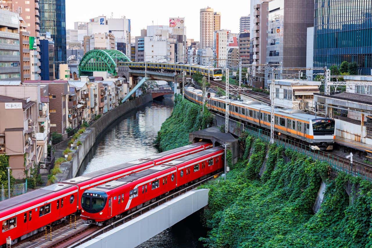 Dois vagões do metrô de Tóquio, vermelhos, cortando a paisagem da cidade