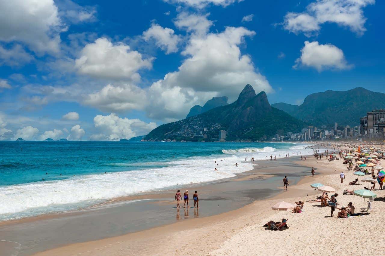 Praia de Ipanema com muitos banhistas e guarda-sóis e o Morro dos Dois Irmãos ao fundo