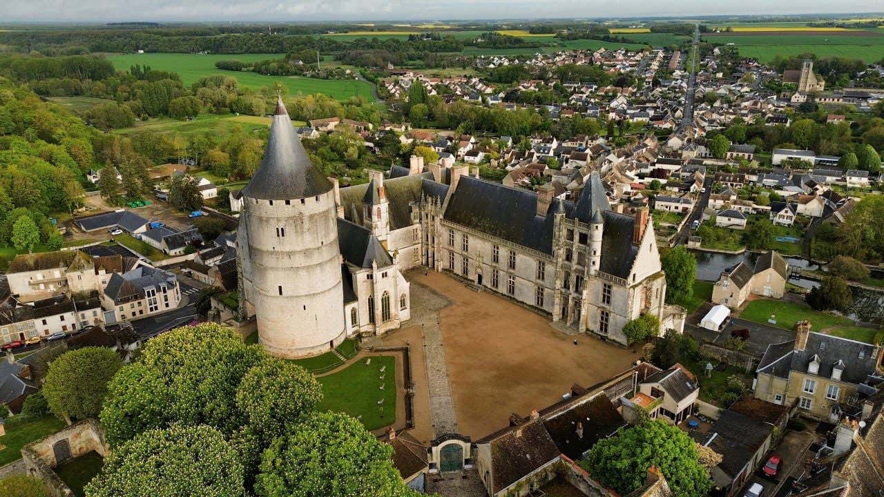 An aerial view of the Château de Châteaudon surrounded by a village, greenery, and roads.