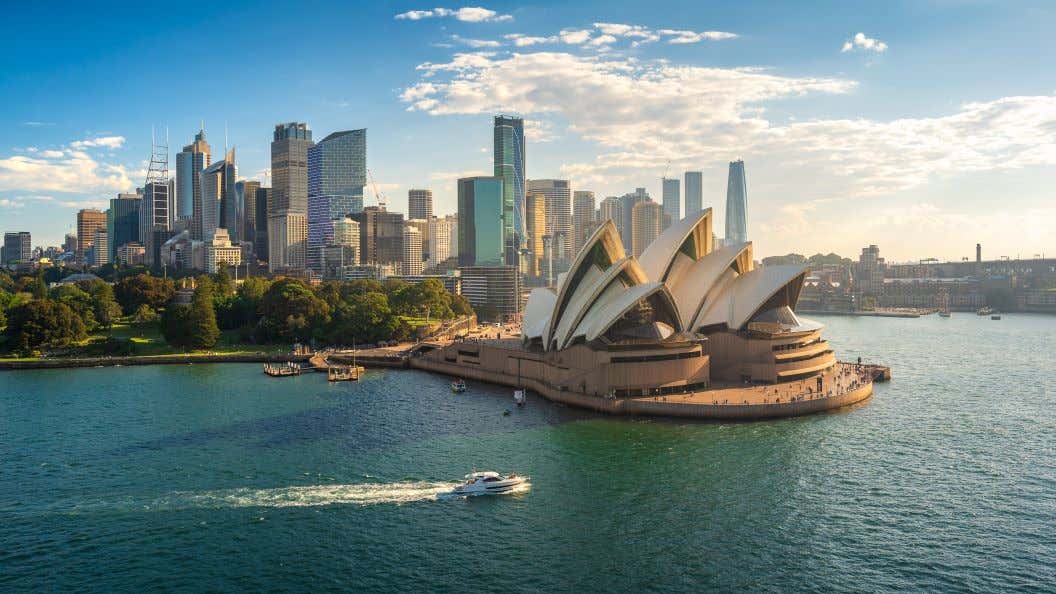 A view of the Sydney Opera House and skyscrapers behind under a blue sky with clouds