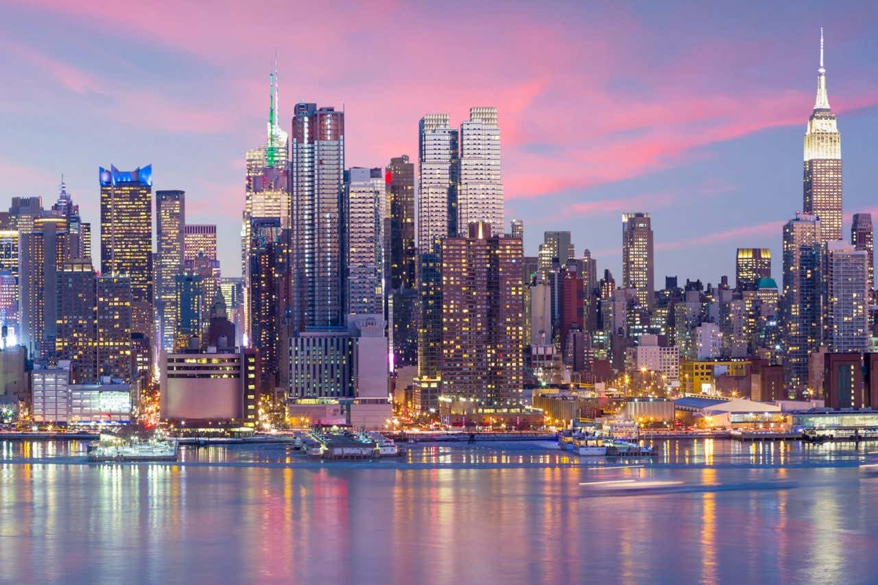 I grattacieli di New York fotografati al tramonto dal fiume Hudson, con le luci elettriche che escono dalle finestre per riflettersi sull'acqua
