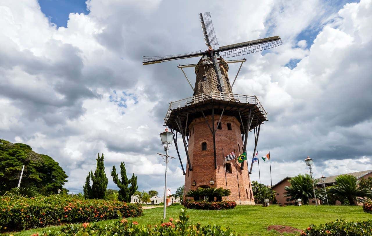 Panorâmica do Moinho dos Povos Unidos em Holambra rodeada de vegetação e flores em um dia nublado