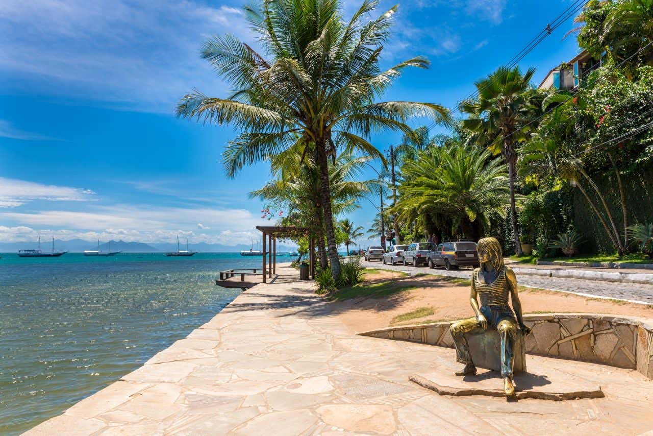 Orla Bardot em Búzios, com a estátua de Brigitte Bardot e diversas palmeiras em um dia ensolarado