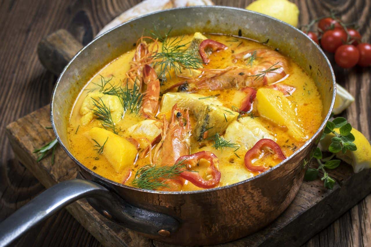 Uma panela com moqueca de peixes, camarões, batata, pimenta e alecrim
