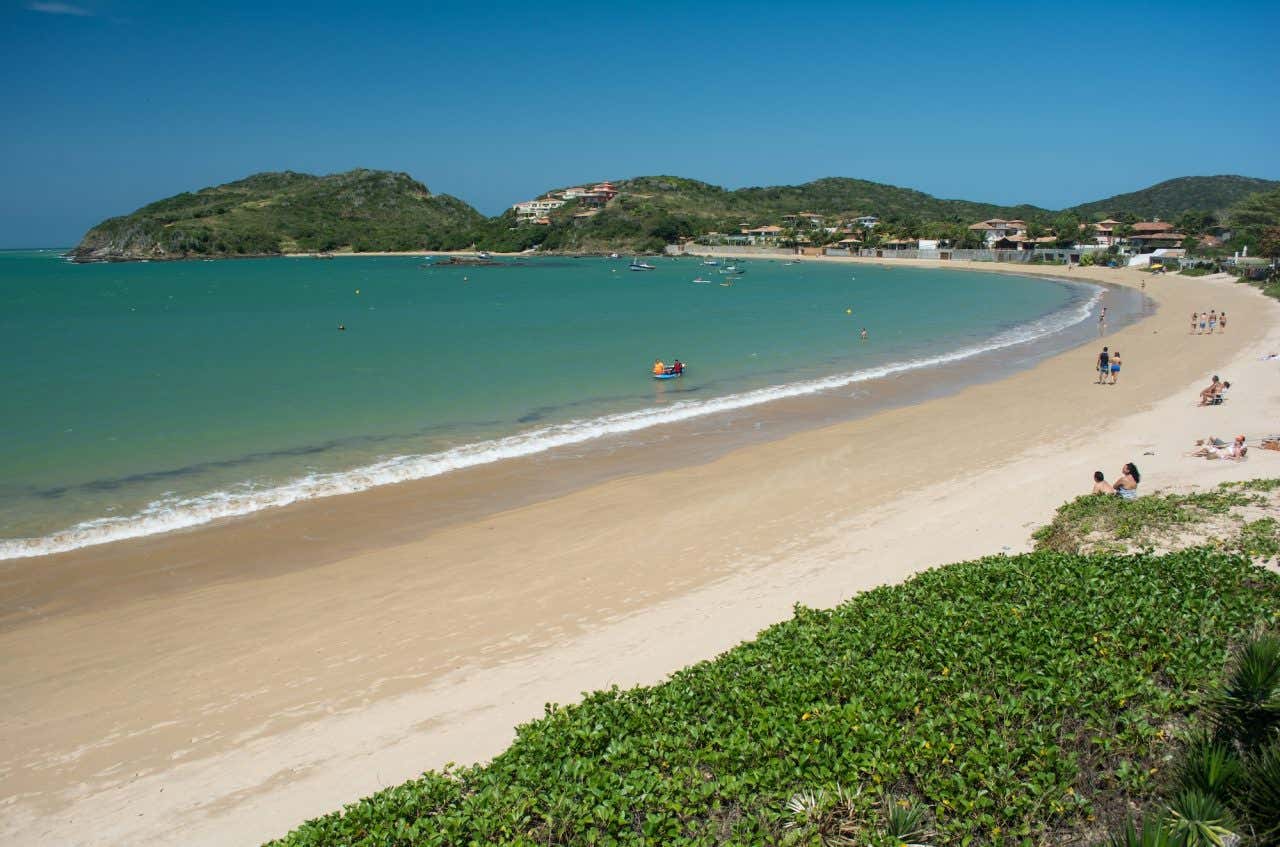 Praia de águas turquesas e areias brancas com colinas ao fundo em um dia ensolarado