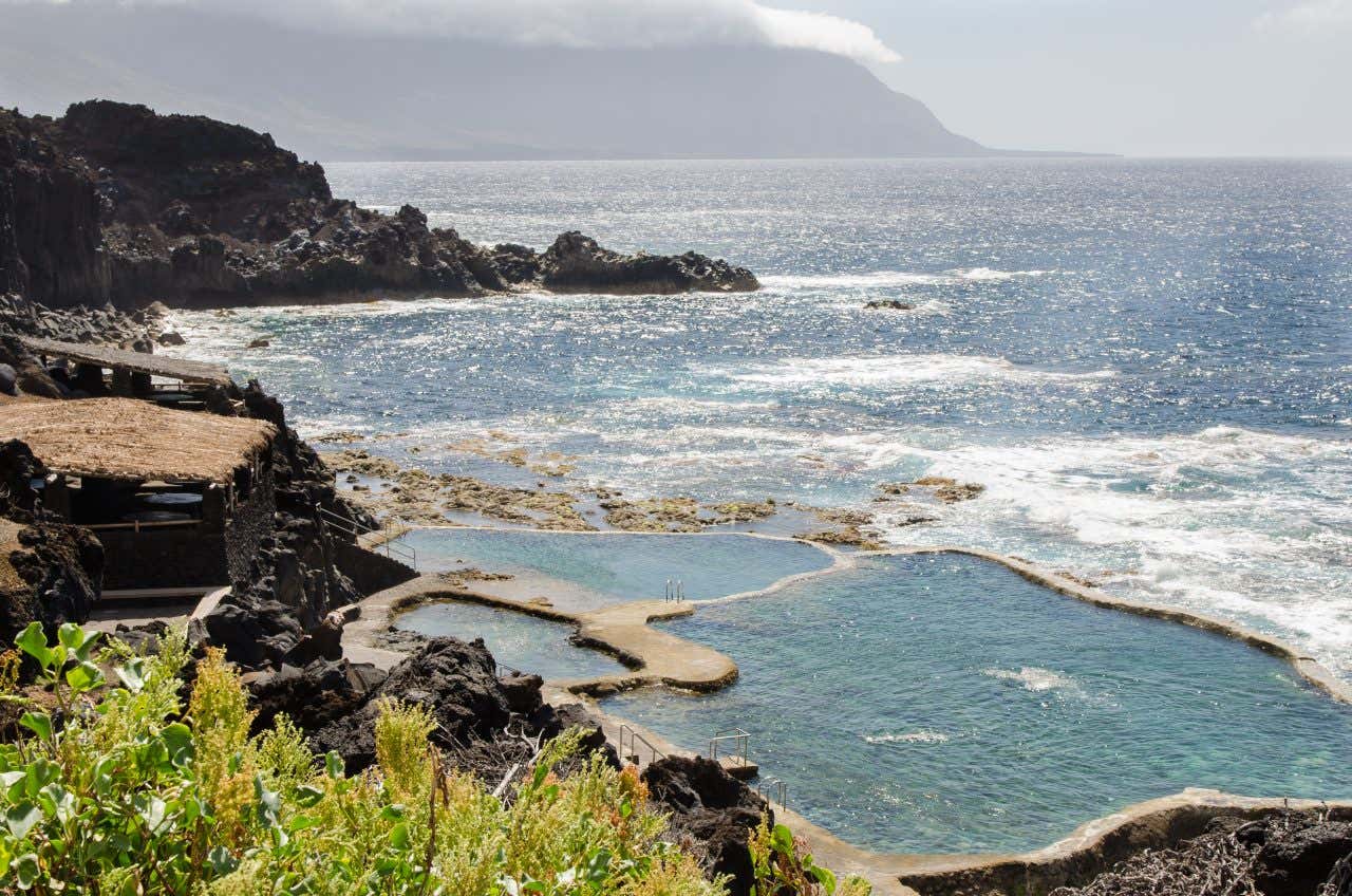 La Maceta natural pools and vegetation, with cliffs in the distance, on a sunny day.