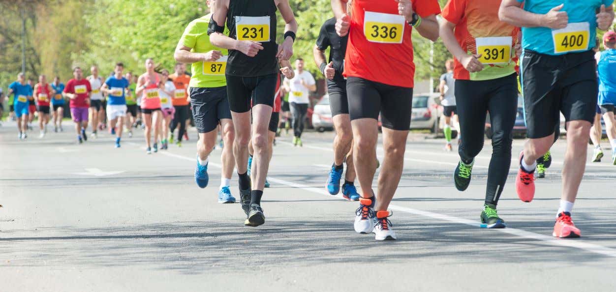 A group of people running a road marathon wearing yellow bibs