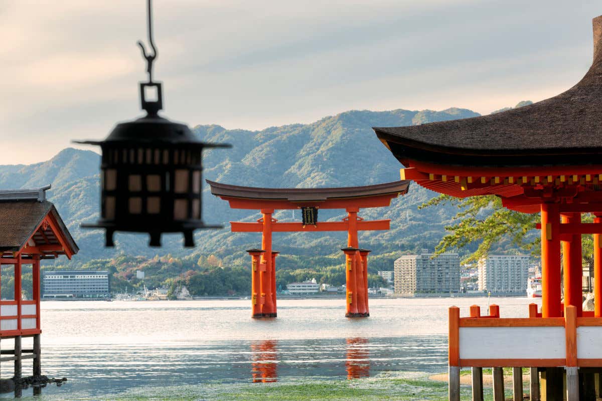El santuario de Itsukushima con varias edificaciones de color rojizo en mitad del mar y frente a unas montañas