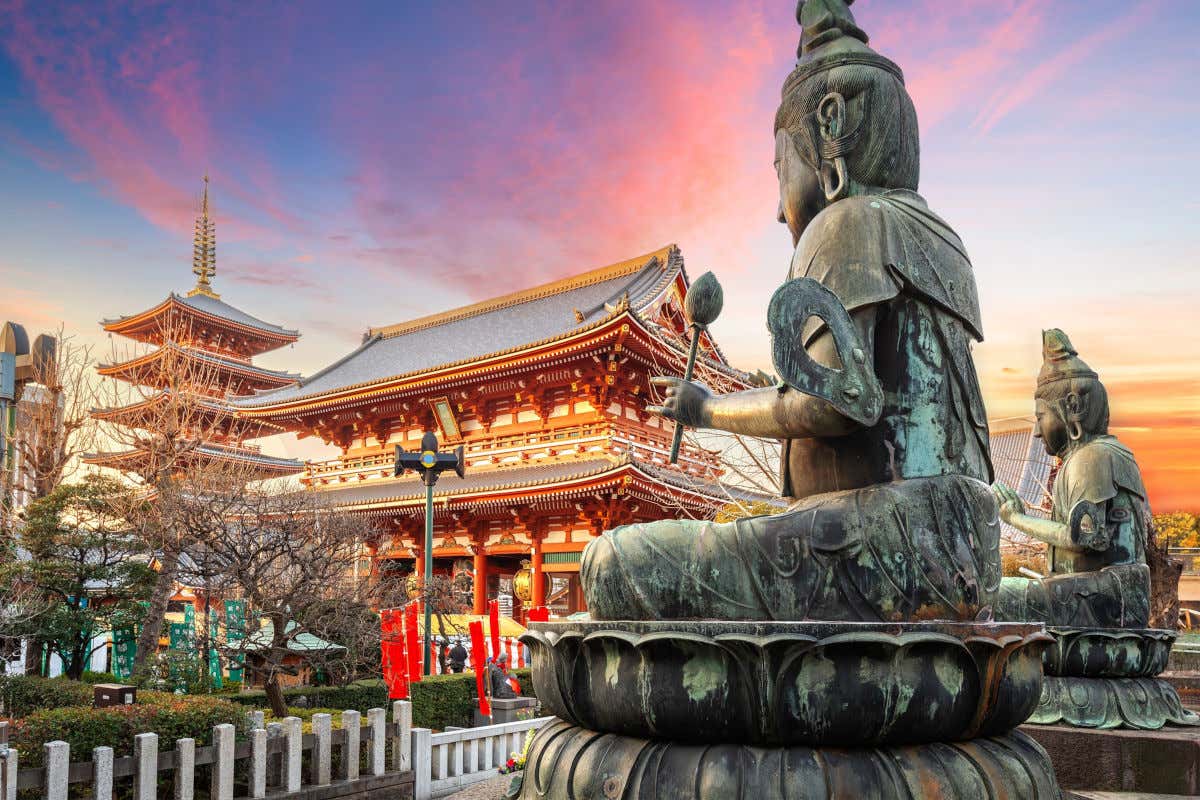 Unas esculturas budistas frente a dos templos de Tokio al atardecer