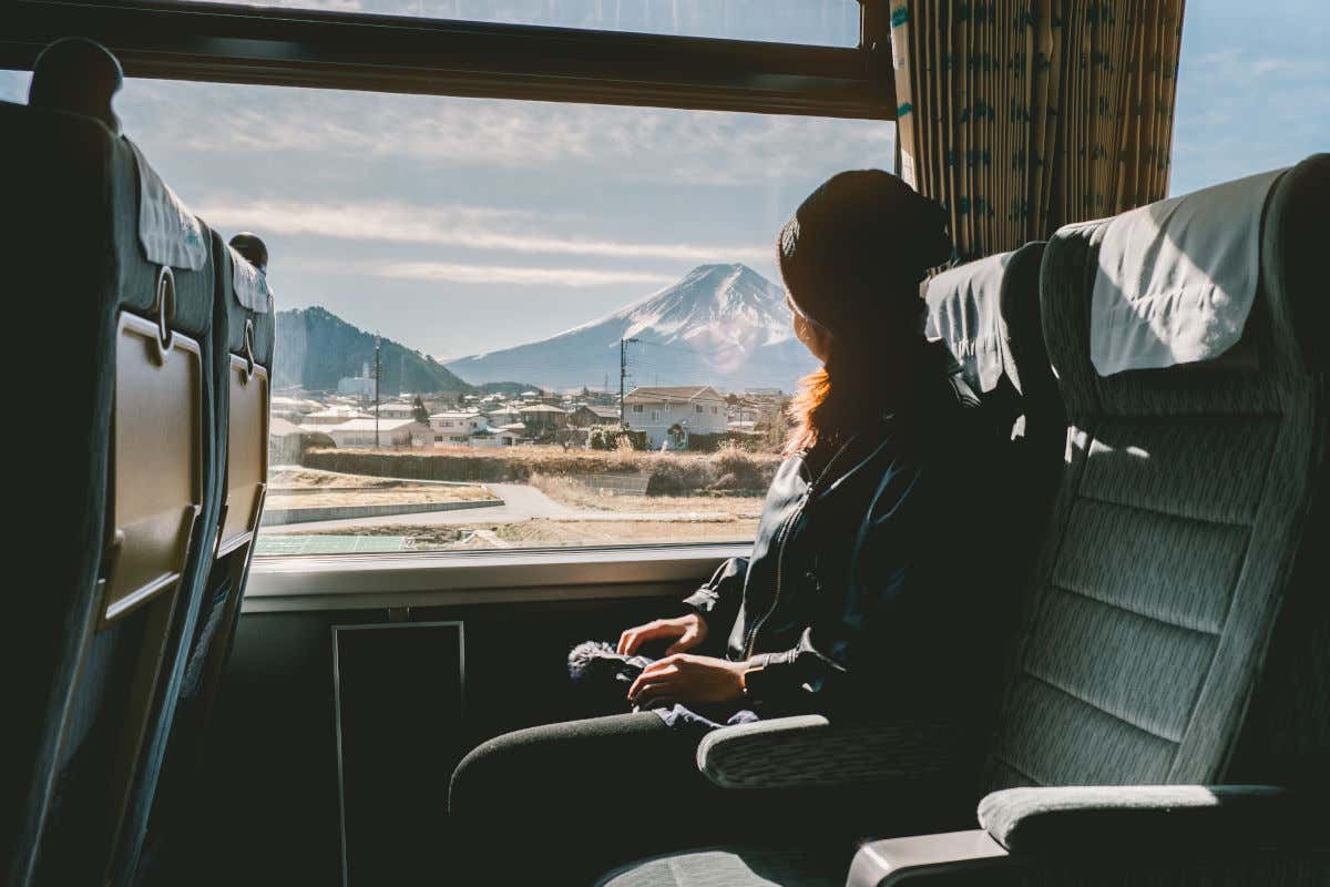 Una mujer sentada en un tren de Japón y contemplando a través de la ventanilla el monte Fuji nevado