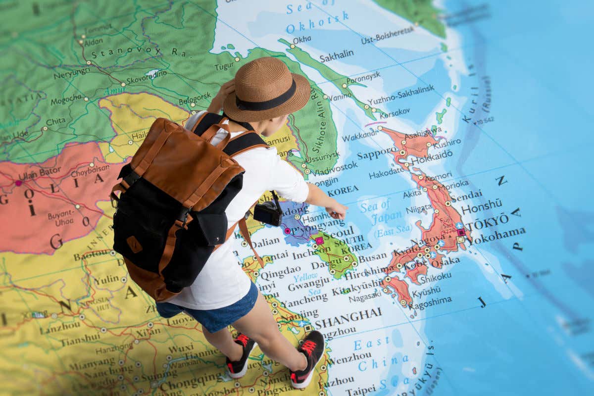 Un turista con mochila contemplando un gigantesco mapa del mundo y apuntando con su mano a Japón