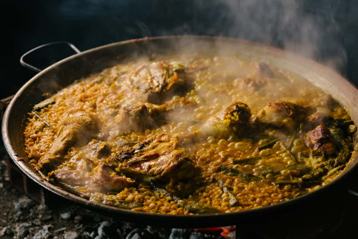 Plato de paella valenciana cocinándose a fuego lento