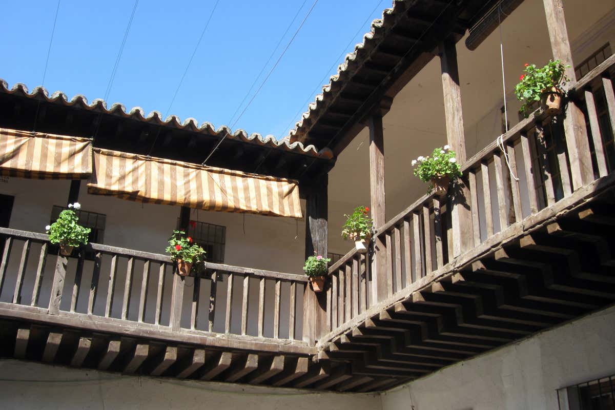 Balcón de madera de un patio, con unas macetas con geranios colgando en algunas partes
