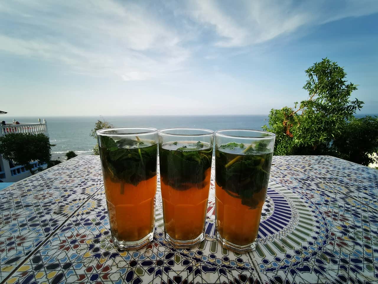 Tres vasitos de té sobre una mesa y el mar de fondo