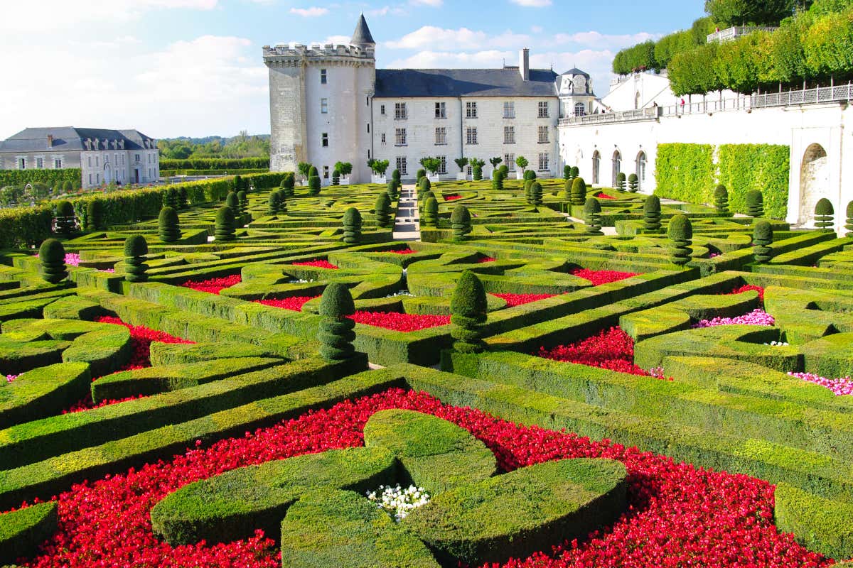 Jardines de estilo francés con rosas rojas y setos verdes frente a los pies de un castillo