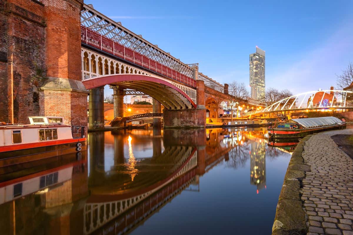 Un barco navegando por un canal de Mánchester compuesto por varios puentes y vigas de ladrillo