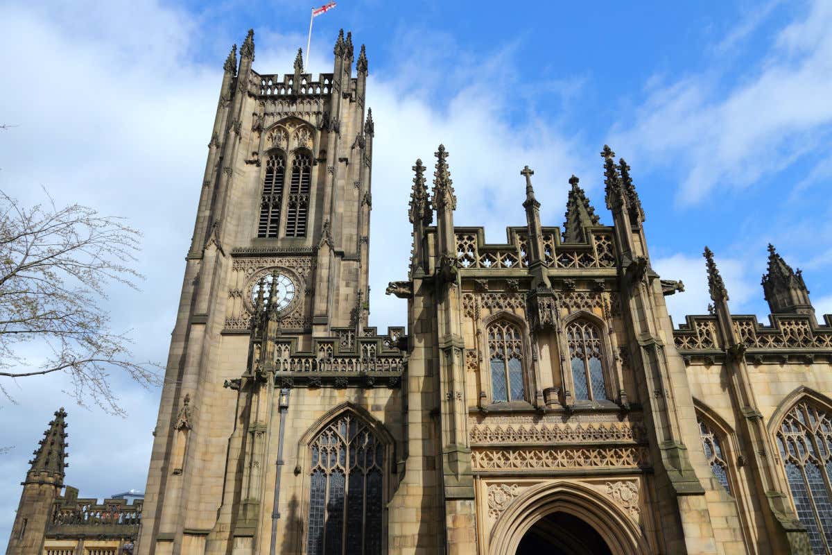 Fachada de la catedral de Mánchester, un templo medieval con numerosos pináculos y con una torre con un reloj analógico