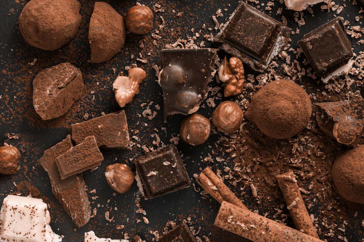 Diferentes porciones de chocolate de varios sabores sobre una tabla de pizarra y acompañados de avellanas, cacao en polvo y ramas de canela