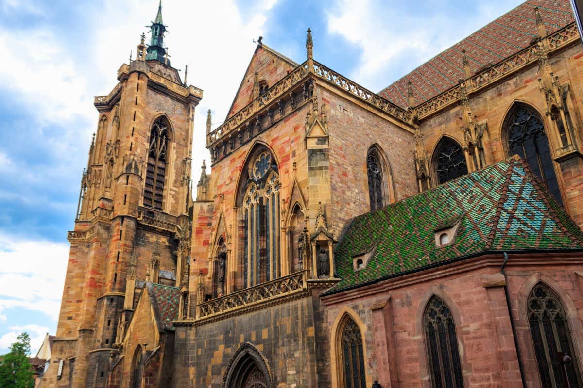 Fachada de una gran iglesia de piedra de Colmar decorada con varias vidrieras y tejas de vivos colores