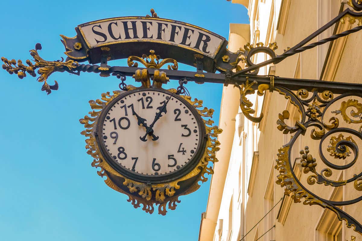 Un reloj analógico decorando la fachada de una casa en una calle comercial