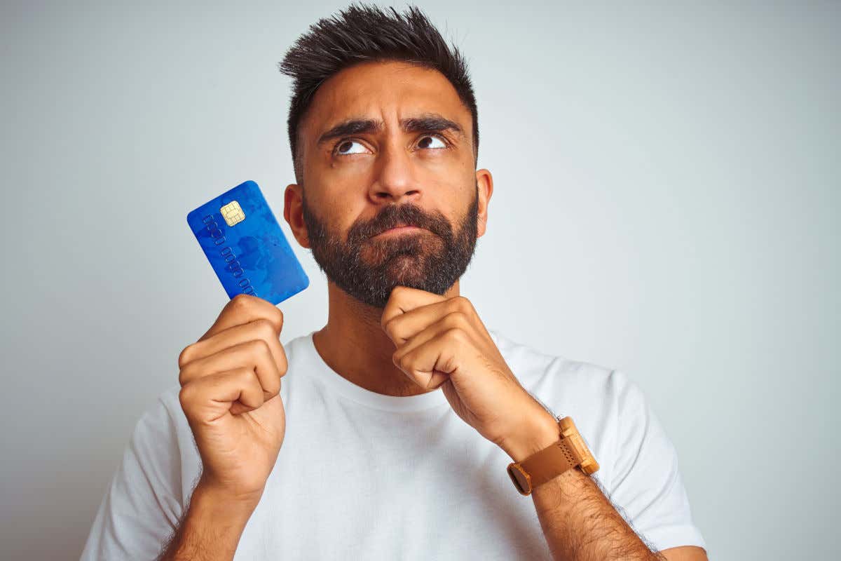 Un hombre con una tarjeta de crédito en la mano posando con cara dubitativa