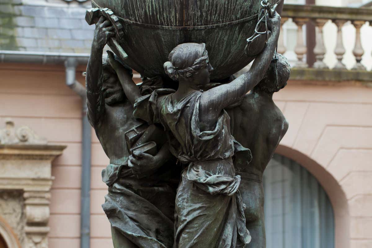 Tres esculturas humanas hechas de bronce sosteniendo una gran esfera en el patio de un museo