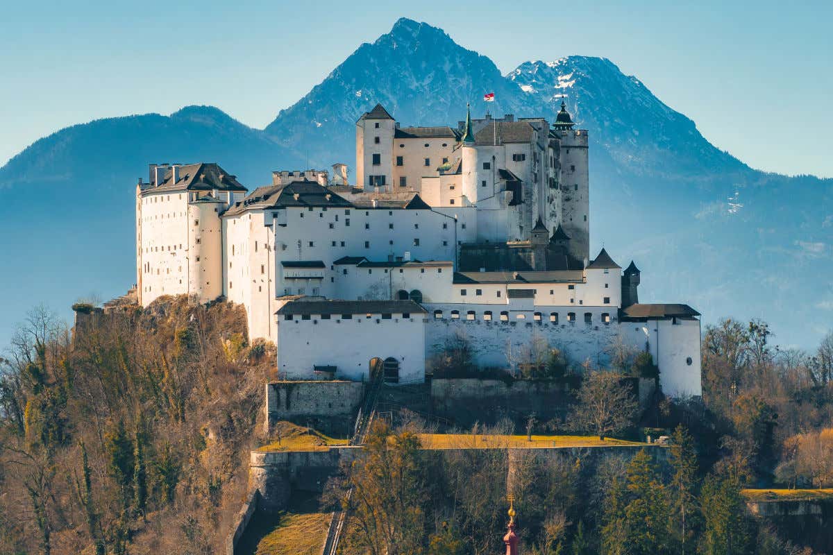 Una fortaleza de Salzburgo con varias torres ubicadas en la cima de una colina y rodeada de otras montañas de mayor tamaño